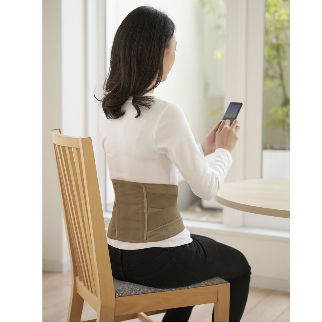 女性坐在椅子上使用手機，穿著輕量雙重承托透氣腰封，顯示舒適的背部支撐。
